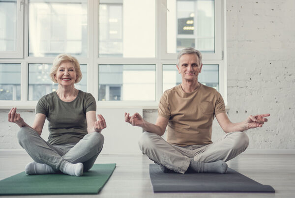 Portrait of cheery aging lady and man sitting on carpets in lotus position and smiling